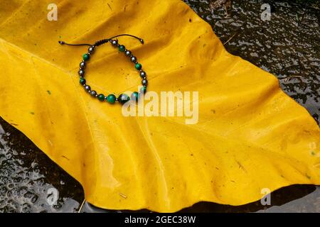 Ein Armband runde Perlen auf gelb grünen Blättern mit Stein hinten Stockfoto