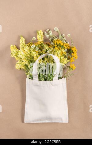 Bouquet von Feldblumen in Stoff Öko-Tasche auf beigem Hintergrund. Konzept kein Kunststoff und kein Abfall. Mockup von oben. Stockfoto