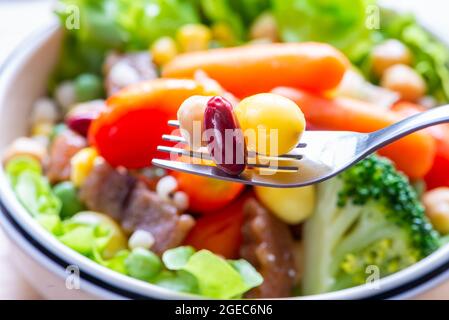 Nahaufnahme rote Bohne, Nuss, Ginkgo biloba auf der Gabel. Verschwommener Hintergrund des Salats. Stockfoto