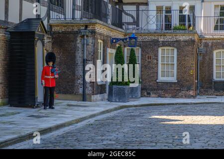 Staycation Idee. Coldstream Guards Wachposten in Militärkleidung mit einer Waffe, die an der Wachtposten-Box vor dem Queen's House am Tower of London angebracht ist. Stockfoto