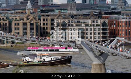 London, Greater London, England, August 10 2021: Boote fahren unter der Millennium Bridge an der Themse mit Gebäuden im Hintergrund. Stockfoto