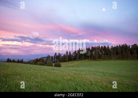 Pastellrosa Sonnenuntergang Wolkenlandschaft über dem Jura-Gebirge. Schöne Abendhimmellandschaft über Wiesen und Wald. Stockfoto