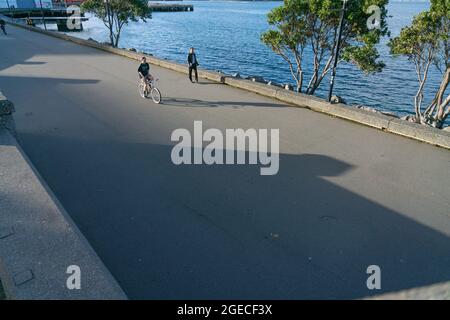 Wellington Neuseeland - 29 2021. Juli; Radfahrer und Spaziergänger fahren entlang der Uferpromenade der Stadt in langen Schatten am späten Nachmittag. Stockfoto