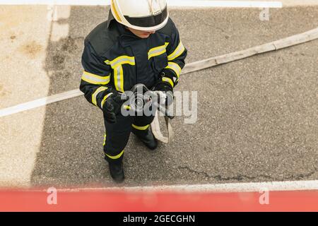 Ein junger Feuerwehrmann in Uniform mit Wasserschlauch bereit für den Einsatz gekleidet Stockfoto