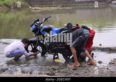 Ländliche Kinder waschen Fahrräder mit Flusswasser, natürliches Grün im Hintergrund Stockfoto