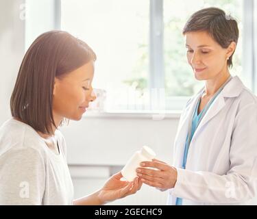 Lächelnde Ärztin mittleren Alters verschreibt Medikamente und gibt dem Patienten eine Flasche Vitamine Stockfoto