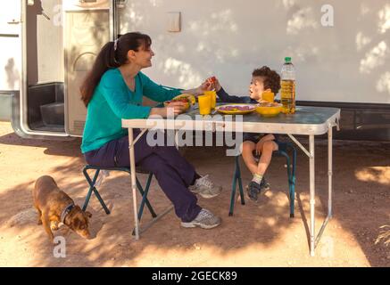 Junge mit seiner Mutter und seinem Welpen, der ein Picknick auf einem Tisch vor dem Wohnheim hat Stockfoto