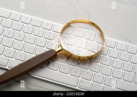 Lupe auf einer Computertastatur. Illustriert eine Suche im Internet. Suchen von Dingen mithilfe eines Computers. Stockfoto