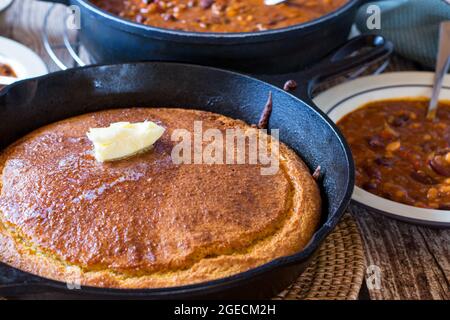 Würziger Bohneneintopf mit frisch gebackenem Maisbrot auf einem Holztisch Stockfoto