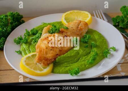 Gebratenes Fischfilet mit grünem Erbsenpüree, serviert mit Zitrone und Parley auf einem Teller. Nahaufnahme und abgelegene Sicht Stockfoto