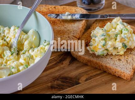 Fettarmer Eiersalat mit Quark, gekochten und gehackten Eiern und Schnittlauch, serviert mit Vollkorn-Toast auf einem Holzbrett. Proteinreiches Gericht Stockfoto
