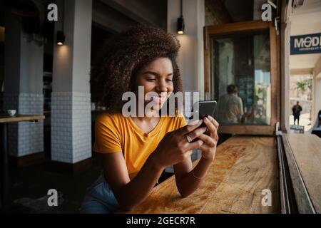 Lächelnde Kundin schreibt Smartphone-SMS-Mitschülern vom Smartphone, das im trendigen Café sitzt Stockfoto