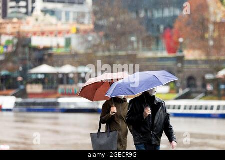 Melbourne, Australien, 14. August 2020. Einheimische mit Sonnenschirmen trotzen dem Wetter, während sie während der COVID-19 in Melbourne, Australien, am Yarra River spazieren. Victoria verzeichnete 14 COVID-bedingte Todesfälle, darunter ein 20-jähriges Kind, das als jüngster in Australien an dem Coronavirus starb, und weitere 372 neue Fälle über Nacht. (Foto von Dave Hewison/Speed Media) Quelle: Dave Hewison/Speed Media/Alamy Live News Stockfoto