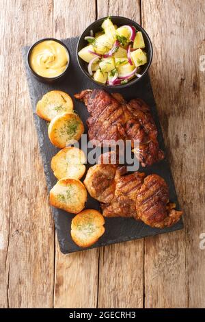 Schwenker oder Schwenkbraten ist ein mariniertes Schweinehals-Steak, das mit Kartoffelsalat, Senf und Toast in der Nähe auf dem Schiefertafel auf dem Tisch serviert wird. Vert Stockfoto