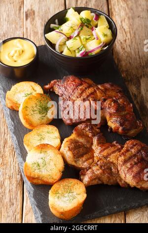 Schwenker oder Schwenkbraten ist ein mariniertes Schweinehals-Steak, das mit Kartoffelsalat, Senf und Toast in der Nähe auf dem Schiefertafel auf dem Tisch serviert wird. Vert Stockfoto