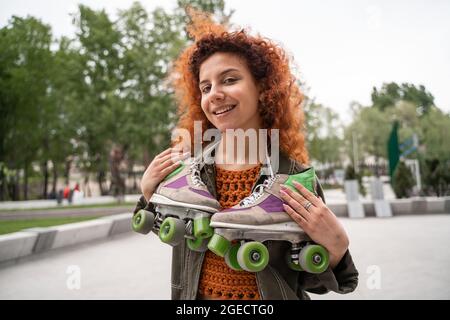 Fröhliche Rothaarige Frau mit Rollschuhe am Hals lächelt draußen vor der Kamera Stockfoto