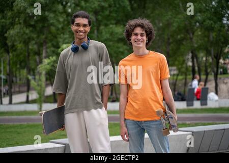 Fröhliche interrassische Freunde mit Skateboards, die draußen vor der Kamera lächeln Stockfoto