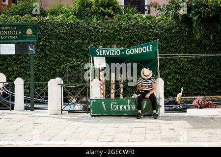 Gondoliere schaut auf das Handy, das auf Touristen in einem leeren Venedig wartet Stockfoto