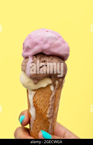Die Hand einer Frau hält einen Eiskegel, der auf einem gelben Hintergrund schmilzt Stockfoto