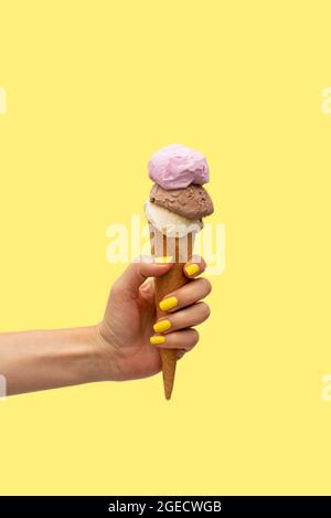 Die Hand der Frau hält ein Eis auf gelbem Hintergrund Stockfoto