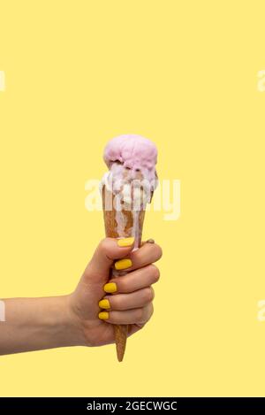Die Hand einer Frau hält einen Eiskegel, der auf einem gelben Hintergrund schmilzt Stockfoto