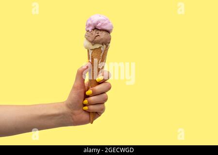 Die Hand einer Frau hält einen Eiskegel, der auf einem gelben Hintergrund schmilzt Stockfoto