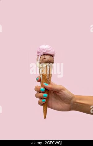 Die Hand einer Frau hält einen Eiskegel, der auf einem rosa Hintergrund schmilzt Stockfoto