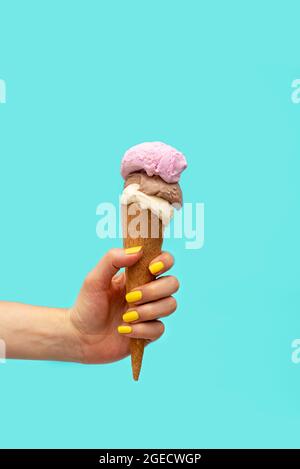 Die Hand der Frau hält ein Eis auf einem hellblauen Hintergrund Stockfoto