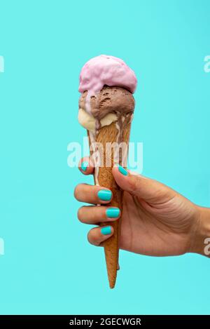 Die Hand einer Frau hält einen Eiskegel, der auf einem hellblauen Hintergrund schmilzt Stockfoto