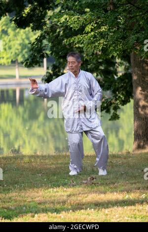 Ein Mann mittleren Alters in traditioneller Tai Chi Kleidung übt in einem Park in Queens, New York City. Stockfoto