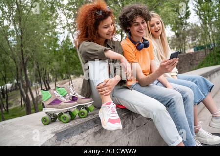 Fröhlicher Skater mit Handy in der Nähe lächelnder Freunde im Freien Stockfoto