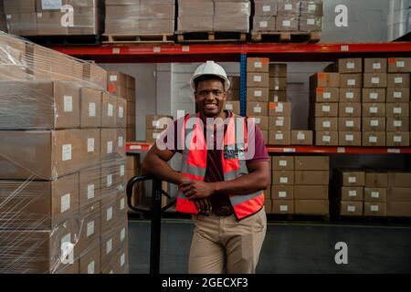 Ein lächelnder Arbeiter lehnte sich fröhlich gegen Pakete, die an die Kunden geliefert werden können Stockfoto