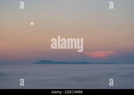 Vollmond fällt und der Nebel in der Morgenzeit. Die Farbe orange Himmel spiegelt die Strahlen der Sonne. Stockfoto