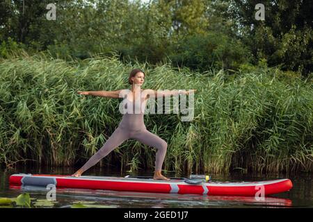 Ein junges kaukasisches, schönes, schlankes Mädchen, das Yoga macht, Pilates auf dem Paddle Board, SUP allein am Sommermorgen. Aktives Leben, Sport, Freizeitbeschäftigung Konzept Stockfoto