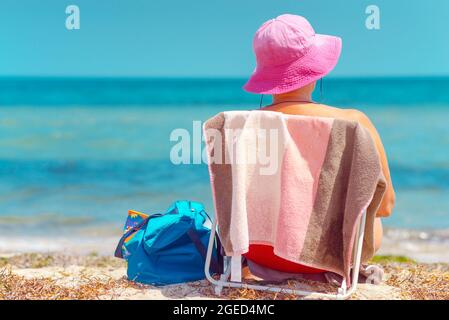 Körperpositive ältere Frau, die auf einem Stuhl am Strand sitzt Stockfoto