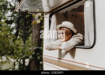 Hübsche junge Frau, die morgens durch das Fenster des Campingwagens schaute. Stockfoto