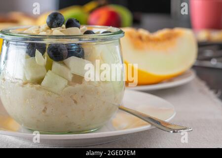 Hafer über Nacht mit frischer Honigmelone und Blaubeeren auf dem Küchentisch. Nahaufnahme und Vorderansicht Stockfoto