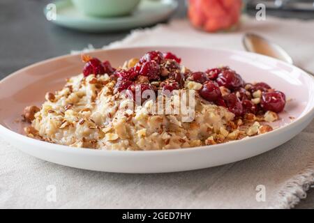 Gesundes Frühstück mit frisch gekochtem und hausgemachtem Brei, Nüssen, Leinsamen, Honig und Sauerkirschen Stockfoto