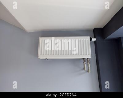 Weißer Heizkörper mit Thermostat an grauer Wand. Moderne Kunststoff-Heizrohre. Installation von Heizsystemen. Stockfoto