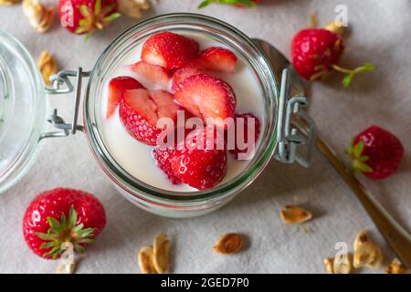 Erdbeeren in einem Glas mit Milch auf hellem Holzhintergrund. Draufsicht oder Draufsicht. Bild einer gesunden Ernährung Stockfoto