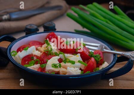 Traditioneller hausgemachter Tomatensalat mit Büffelmozzarella, Olivenöl und Schnittlauch. Serviert in einer Schüssel mit Gabel auf rustikalem und Holztisch Stockfoto