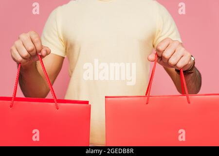 Beschnittene Ansicht eines jungen Mannes, der rote Einkaufstaschen isoliert auf rosa hält Stockfoto