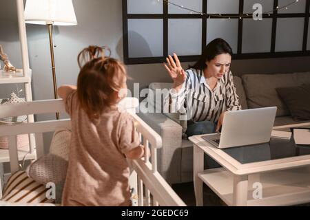 Gestresste Mutter mit kleinem Baby, das spät abends zu Hause arbeitet Stockfoto