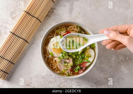 Frau, die leckere chinesische Suppe mit Huhn auf hellem Hintergrund isst, Nahaufnahme Stockfoto