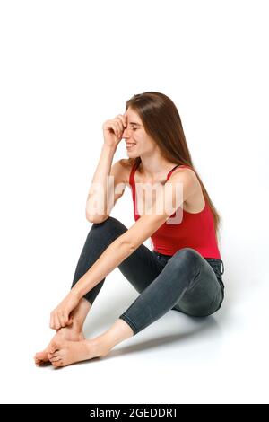 Frau in rotem Tank-Top und Jeans sitzt auf einem Boden und lacht Stockfoto