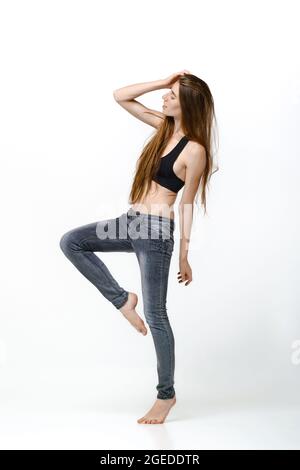 Vollständiges Porträt einer barfuß-jungen Frau im Tank-Top und einer Jeans im Profil Stockfoto