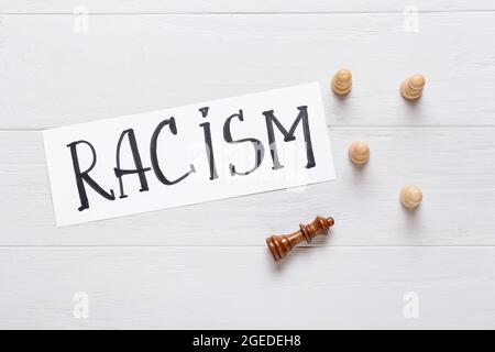 Verschiedene Schachfiguren auf weißem Holzhintergrund. Rassismus-Konzept Stockfoto