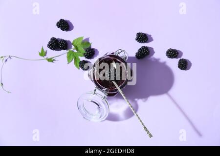 Glas mit leckeren Brombeermarmelade und Beeren auf farbigem Hintergrund Stockfoto