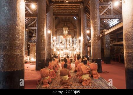 Buddhistische Mönche und Novizen Abendgebet im alten Tempel von Wat Xieng Thong, Luang Prabang, Laos. Weicher Fokus auf Buddha-Statue. Stockfoto