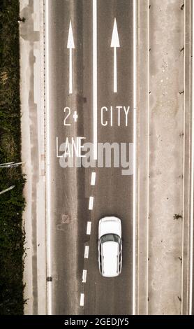 Luftaufnahme eines zweispurigen Straßenschilds, das den Verkehr in Richtung einer Stadt lenkt, mit Maßnahmen zur Verkehrsberuhigung von zwei Personen auf einer Autospur Stockfoto